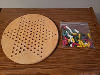 Round wooden Chinese checkers board beside bag of coloured pegs
