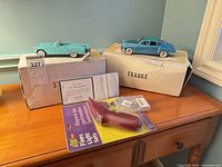 Both diecast cars on their respective boxes with certificate and light repair tool visible