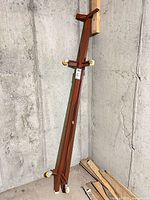 Folded red metal bed frame leaning against wall, showing four casters and surface wear