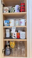 Cabinet view showing multiple shelves of mugs, tumblers, glass mugs, teapot
