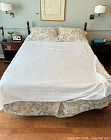 Front view of made queen bed showing headboard, bedding, mattress on mahogany frame