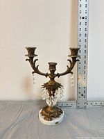 Front view of brass candelabra showing three arms, crystal drops, marble base and ruler for scale