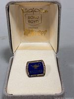 Pin in open Bond Boyd box showing markings and face design