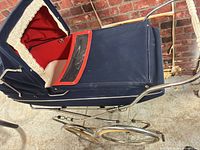 Side view of navy blue pram showing chrome frame, wheels, navy canopy, red interior