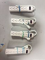 Four identical white 6-outlet power strips bundled with elastic bands