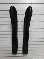 Full view of both black plastic skis hung vertically