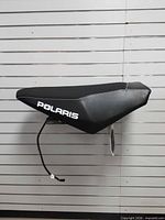 Side profile of Polaris black snowmobile seat with logo and wiring lead visible