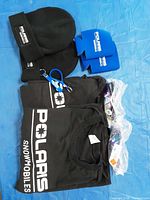 All 10 items laid out: 2 T-shirts, 2 beanies, 2 koozies, 2 sunglasses, 2 keyring lanyards