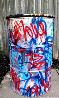 Front view of graffiti-covered steel drum showing blue and red tags and drips
