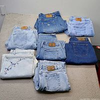 Seven folded jeans laid out showing front waistbands and patches