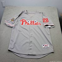 Full view of grey Phillies jersey with front graphics, number 28, World Series patch, Majestic tag