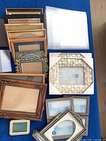 Stacked assortment of wooden, metal, shell inlay and plastic frames plus clear stands shown on blue surface