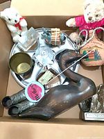 Top view of box showing majority of items including hubcap, wooden duck, bears, candlestick, brass cup, boots, log cabin, donkey, plaque