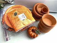 Stacked terracotta saucers and pots with sealed Halloween plates/napkins and ceramic pumpkin