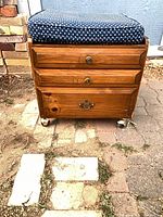 Front view of oak storage bench showing three drawers, cushion and casters