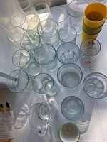 Group of assorted clear glass tumblers, glass pitcher, yellow plastic tumblers, cartoon pint glass and ceramic cup