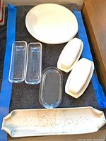 All seven serving pieces arranged on towel: round platter, two glass rectangular trays, oval glass tray, two butter dishes, speckled stoneware platter