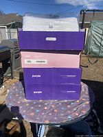 Stack of four Purple Harmony pillow boxes with one pillow in plastic on top