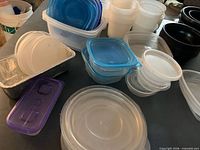 Group of plastic containers, lids, black bowls and aluminum tray