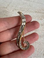 Front view of gold-tone swirl brooch showing baguette and round rhinestones