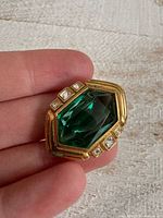 Front view of gold-tone brooch showing green glass center and rhinestones