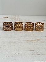 Four brass-plated openwork napkin rings side by side