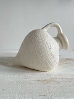 Side view of off-white textured teardrop vase showing handle and spout