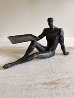 Full view of black metal seated figure holding tray