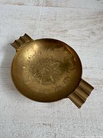 Top view of brass ashtray showing floral etching and rests