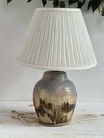 Full view of pottery lamp with white pleated shade and cord