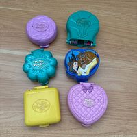 Front view of six Polly Pocket compacts on wood surface