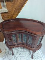 Front view of kidney-shaped curio cabinet under staircase