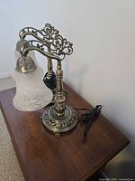 Side view of both ornate metal lamps on table showing scroll arms and bases