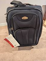 Front view of black Ricardo softside carry-on with tag attached and front zip pockets visible