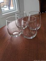 Four clear stemless wine glasses grouped on wooden table