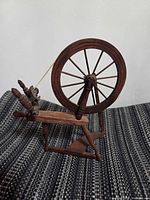 Side view of miniature wooden spinning wheel standing upright on fabric surface