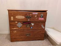 Front view of dresser showing three drawers, brass-tone pulls and stickers