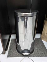Front view of stainless steel step trash can showing cylindrical body and pedal