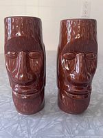Front view of both brown ceramic tiki mugs with Moai faces