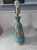 Full view of teal ceramic table lamp showing body shape, gold diamonds, base and bulb