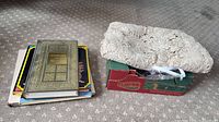 Stack of four books next to folded crocheted tablecloth in box