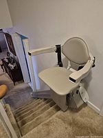 Stairlift chair mounted on rail at top of carpeted staircase