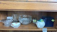 Shelf showing two glass bowls, trinket dish, beer mug, teapot, shakers and blue vase