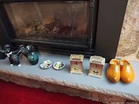 All items lined up: dog figurine, glass pitcher, two Denton candle holders, two Konig brass clocks, wooden clogs
