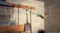 Wall-mounted view of four garden tools: two shovels, cultivator, push broom