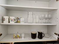 Cupboard shelf showing mugs, pitcher, wine glasses, egg cups, Mikasa creamer & sugar