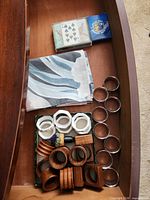 Drawer view showing tablecloth, playing cards, metal napkin rings and boxed assortment of wooden and ceramic rings