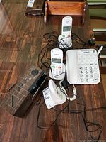Lot overview showing VTech corded phone, three cordless handsets with cradles, Panasonic clock radio and power cords