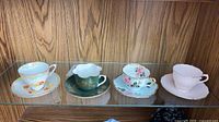 Four teacup and saucer sets on glass shelf