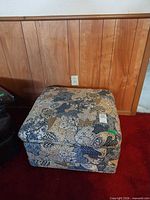 Front view of square paisley upholstered ottoman on red carpet